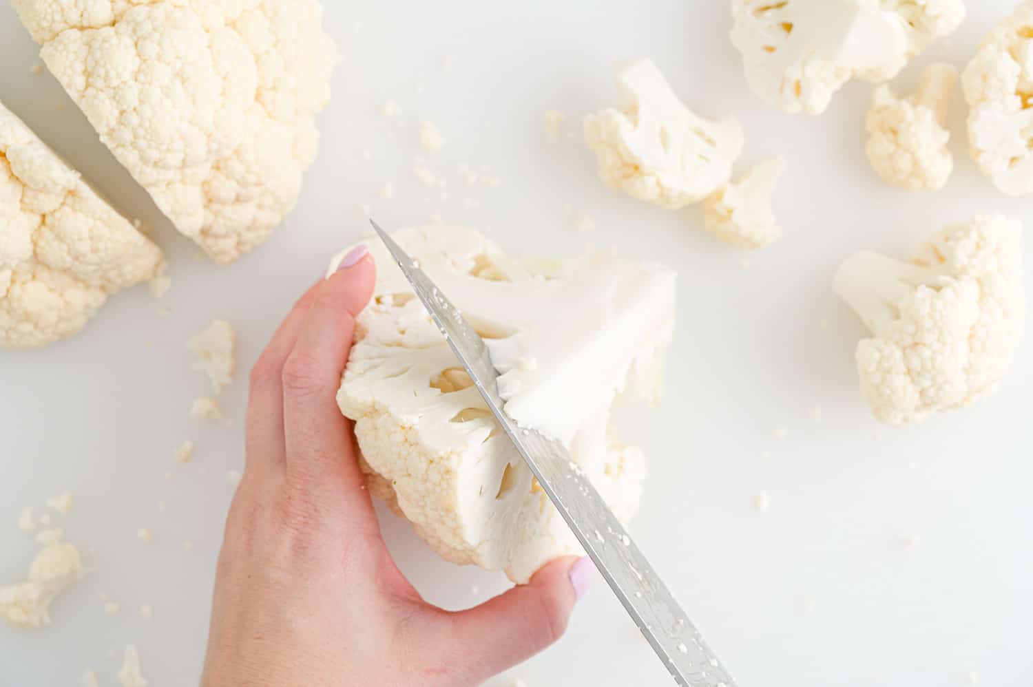Core of cauliflower being cut out of a quarter of a head of cauliflower.