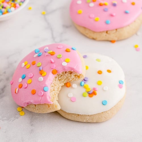 Two frosted cookies, pink and white, pink with a bite taken out.