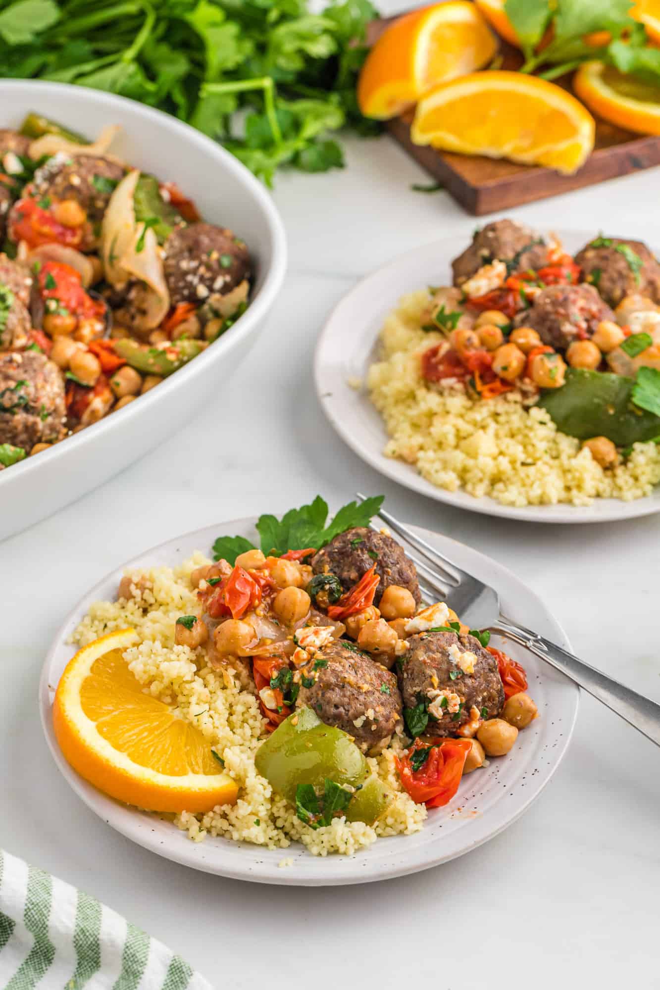 Plated couscous and meatballs with a wedge of orange.