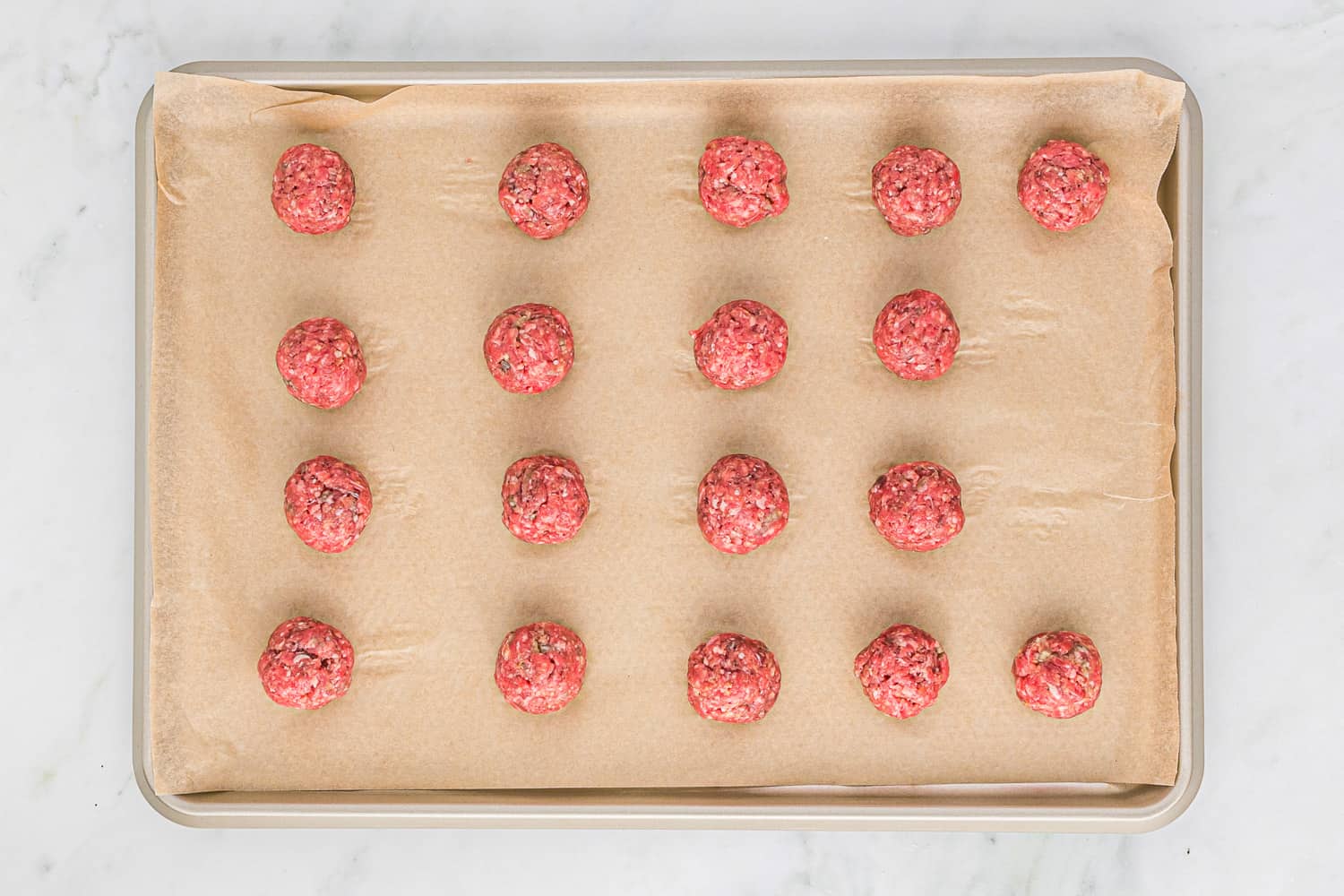 Meatballs formed on a sheet pan.