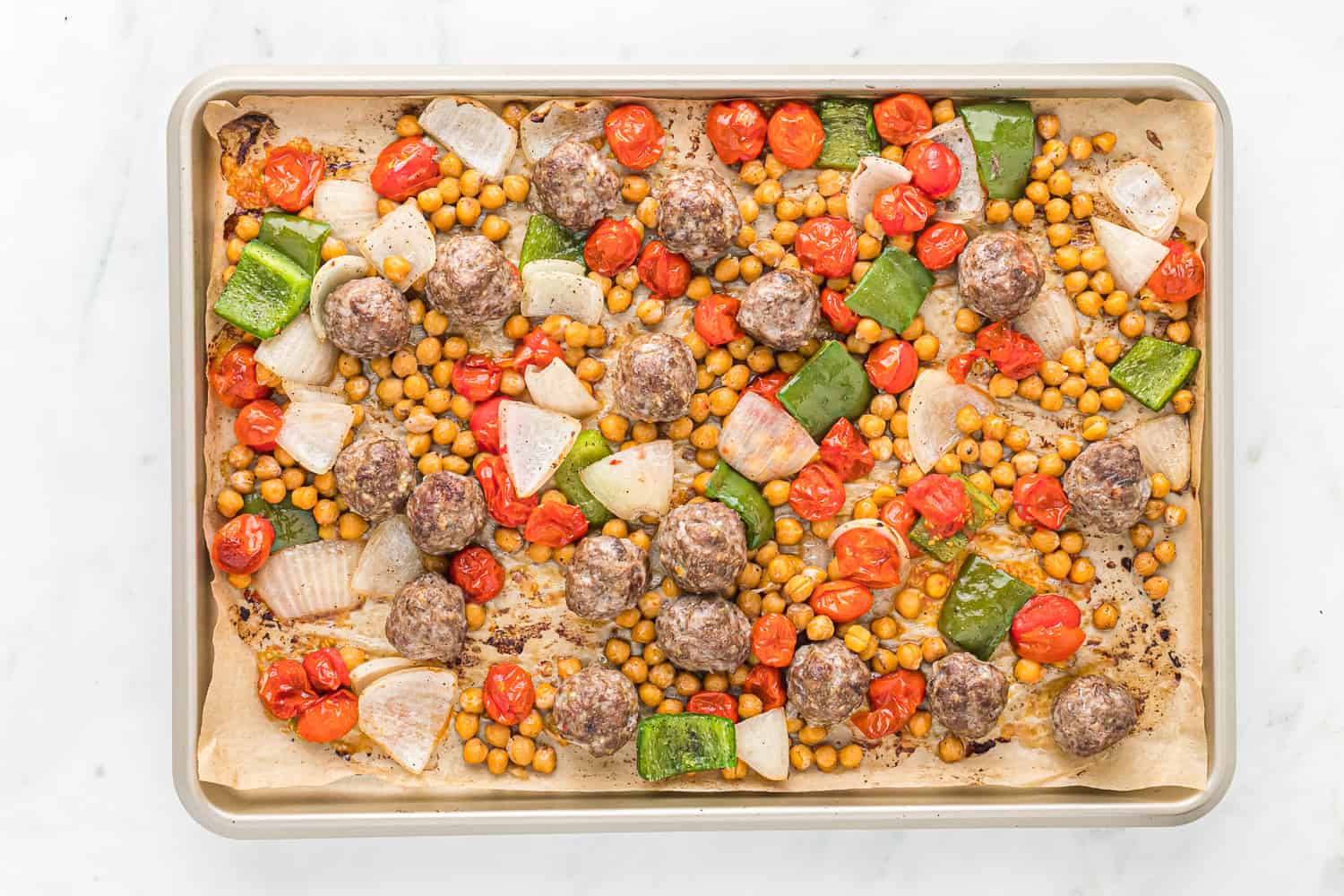 Cooked meatballs and vegetables on a sheet pan.