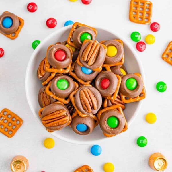 Bowl of rolo pretzels topped with pecan halves and colorful M&Ms.