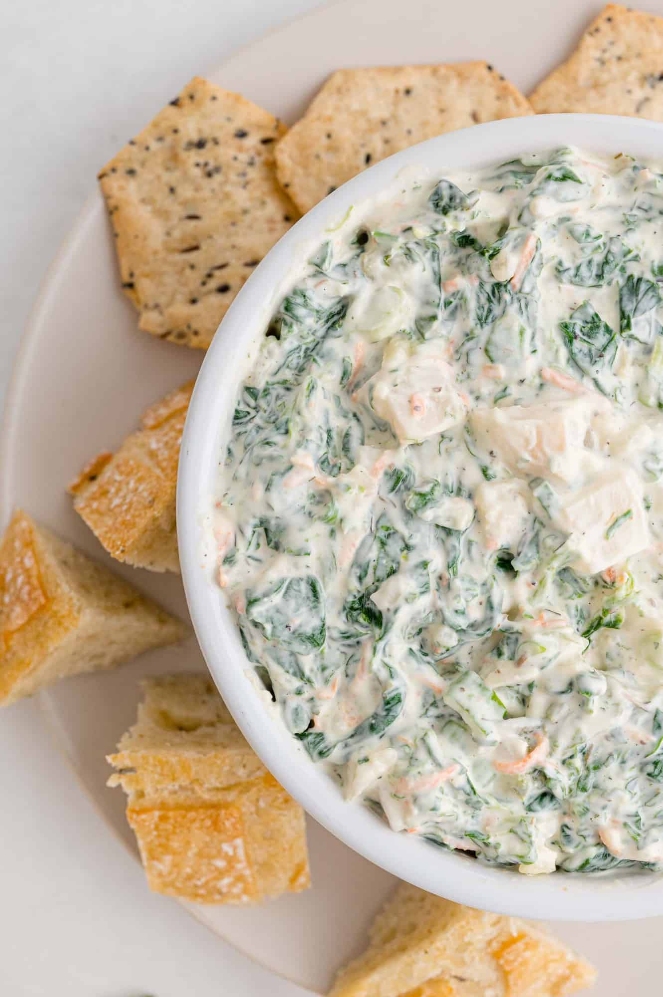 Spinach dip in a bowl surrounded by crackers.