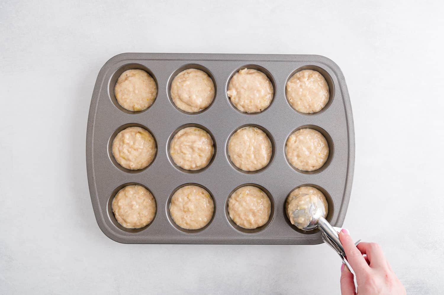 Hand using scoop to put batter in a muffin tin.