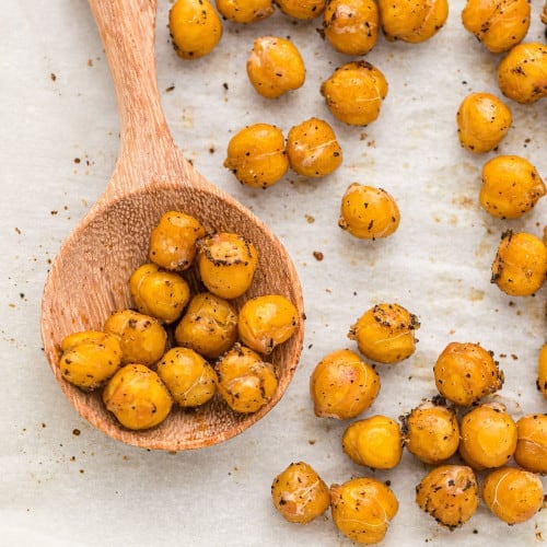 Roasted chickpeas on a wooden spoon, more on parchment lined baking sheet.