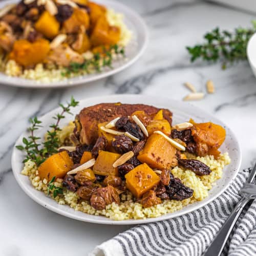 Two plates of chicken, couscous, squash, garnished with almonds.