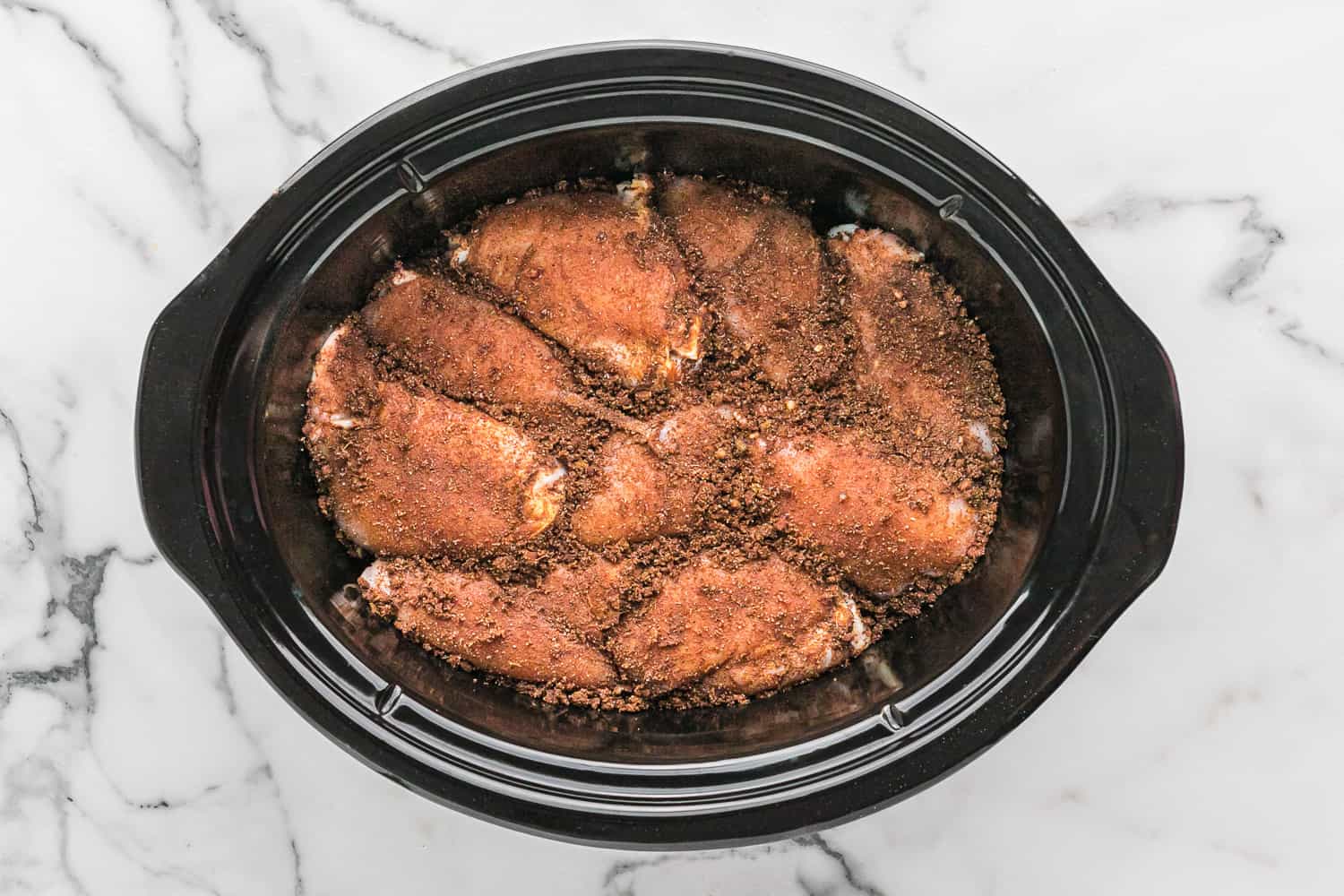 Chicken thighs in slow cooker rubbed with spices.