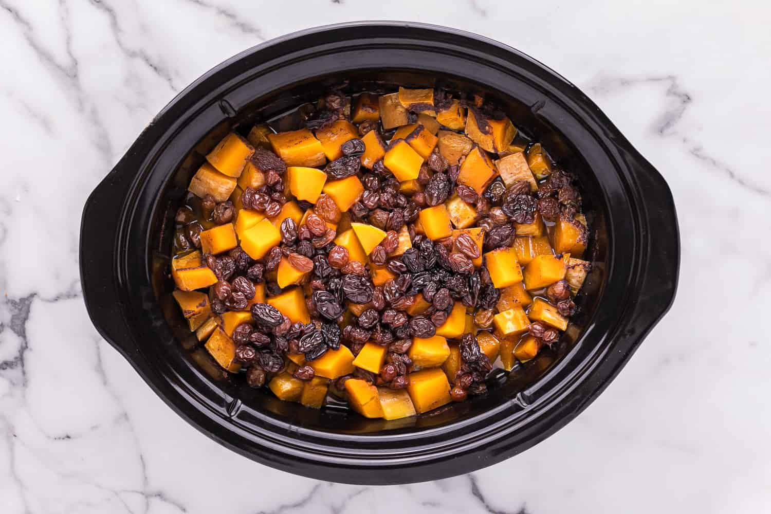 Black slow cooker with squash, chicken, raisins.