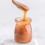 Caramel sauce in a jar, a spoon over it drizzling it into the jar.
