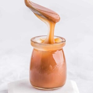 Caramel sauce in a jar, a spoon over it drizzling it into the jar.