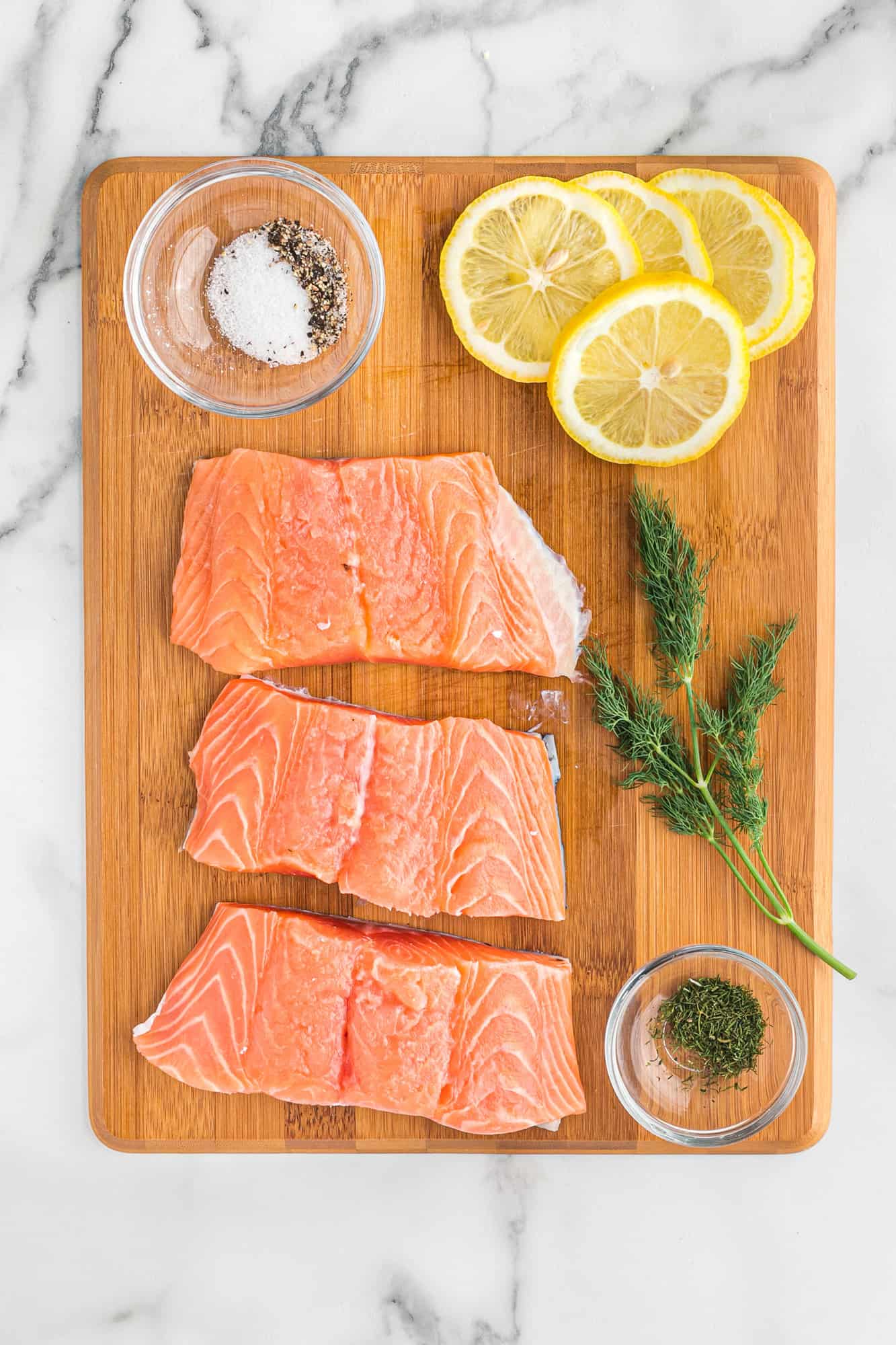 Overhead view of salmon, dill, lemon, salt and pepper.