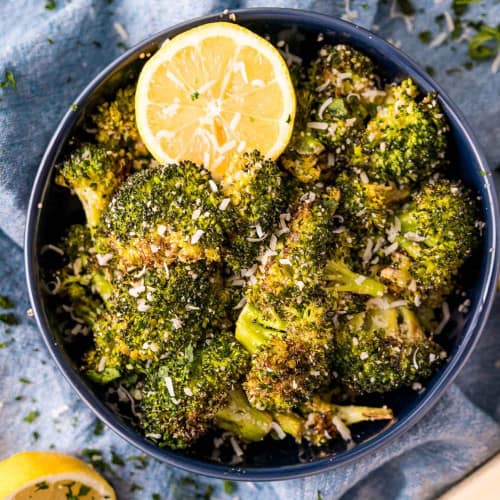 Roasted broccoli with lemon and parmesan in a dark blue bowl.