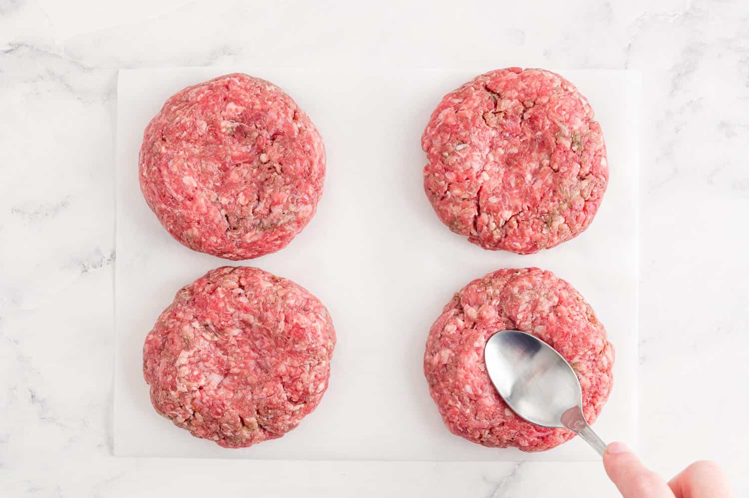 Spoon pressing an indentation in the center of raw burger.