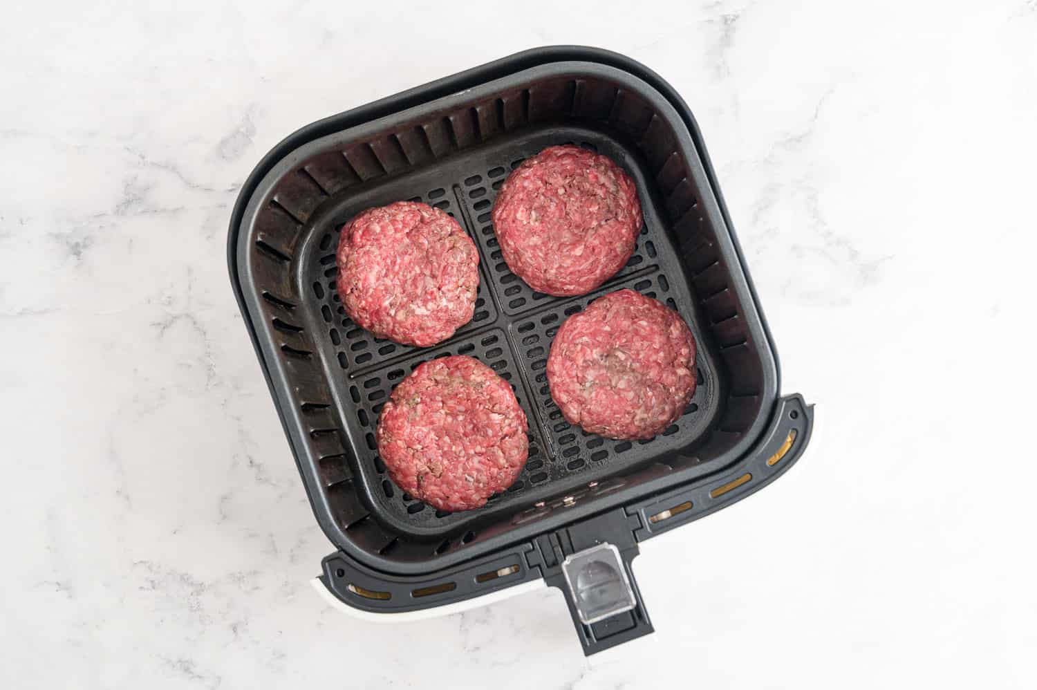 Raw burgers in an air fryer.