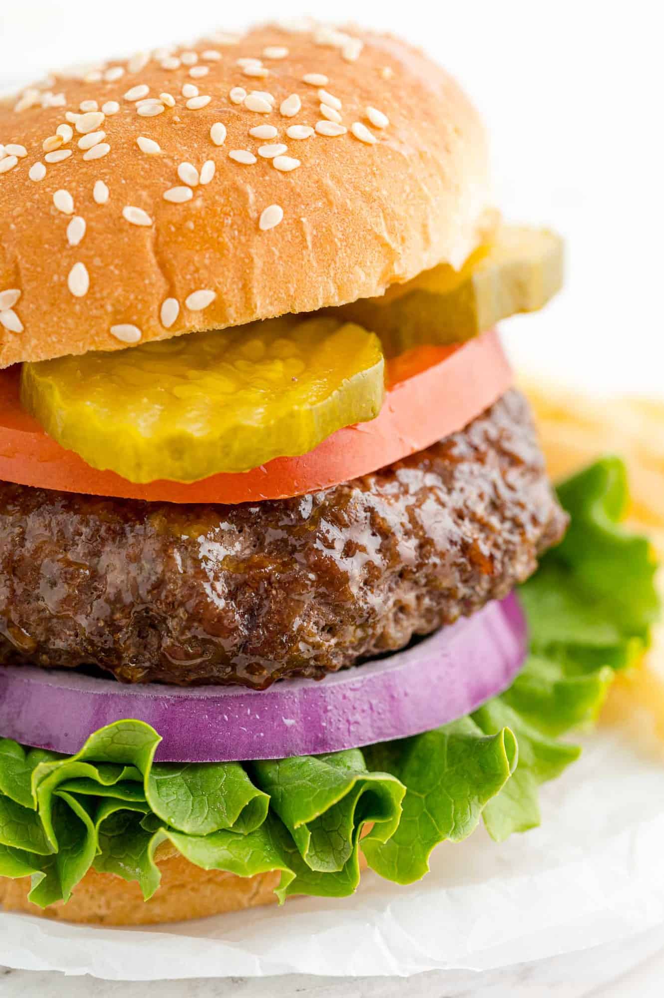 Burger on a sesame seed bun with pickles, tomato, onion, and lettuce.