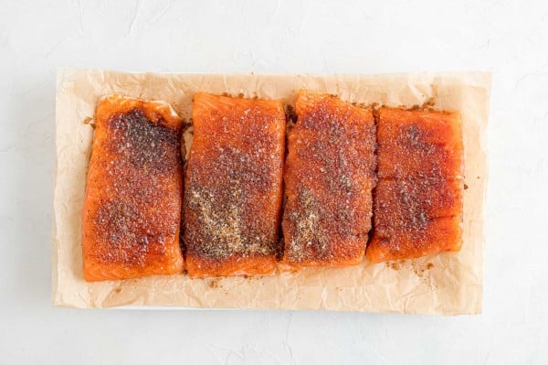 Four BBQ salmon fillets on a parchment-lined plate.