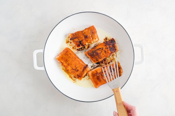 Flipped salmon fillets searing skin-side down in a skillet.