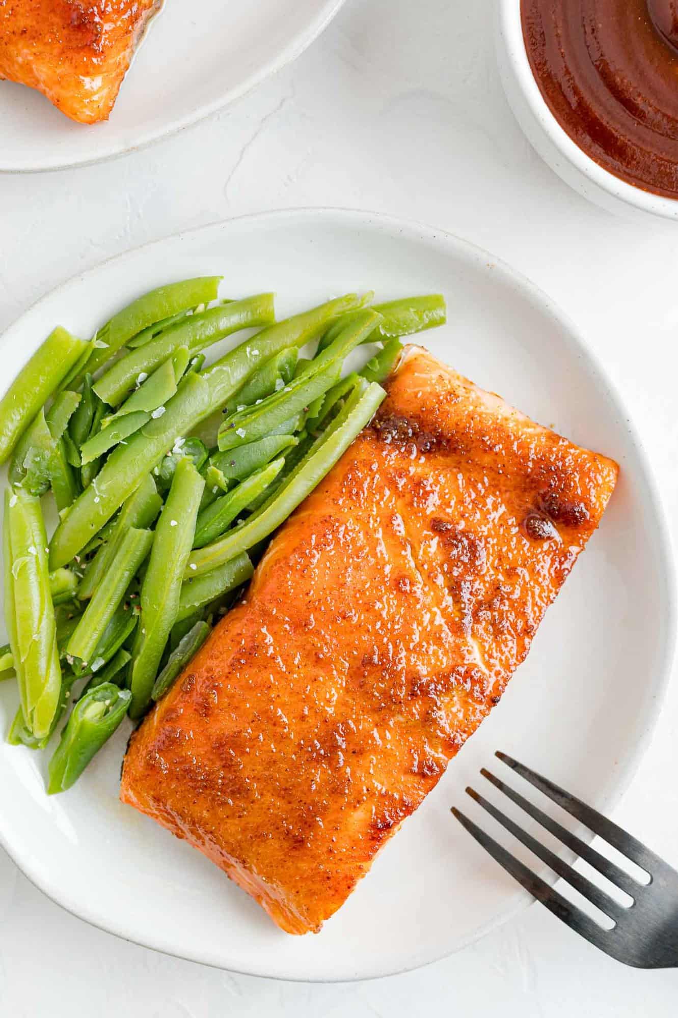 BBQ salmon on a plate with green beans, next to a fork.