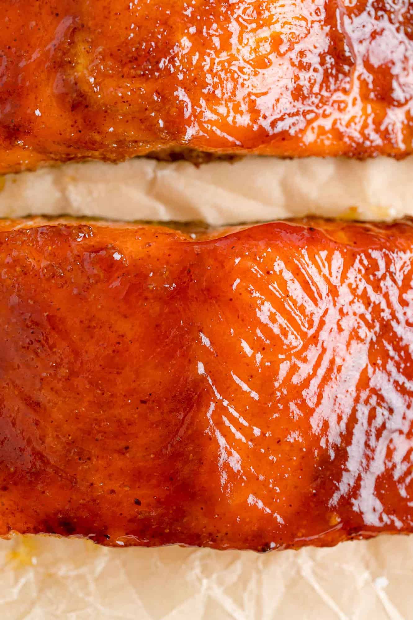 Close up of BBQ salmon fillets glazed with barbecue sauce on a piece of parchment paper.