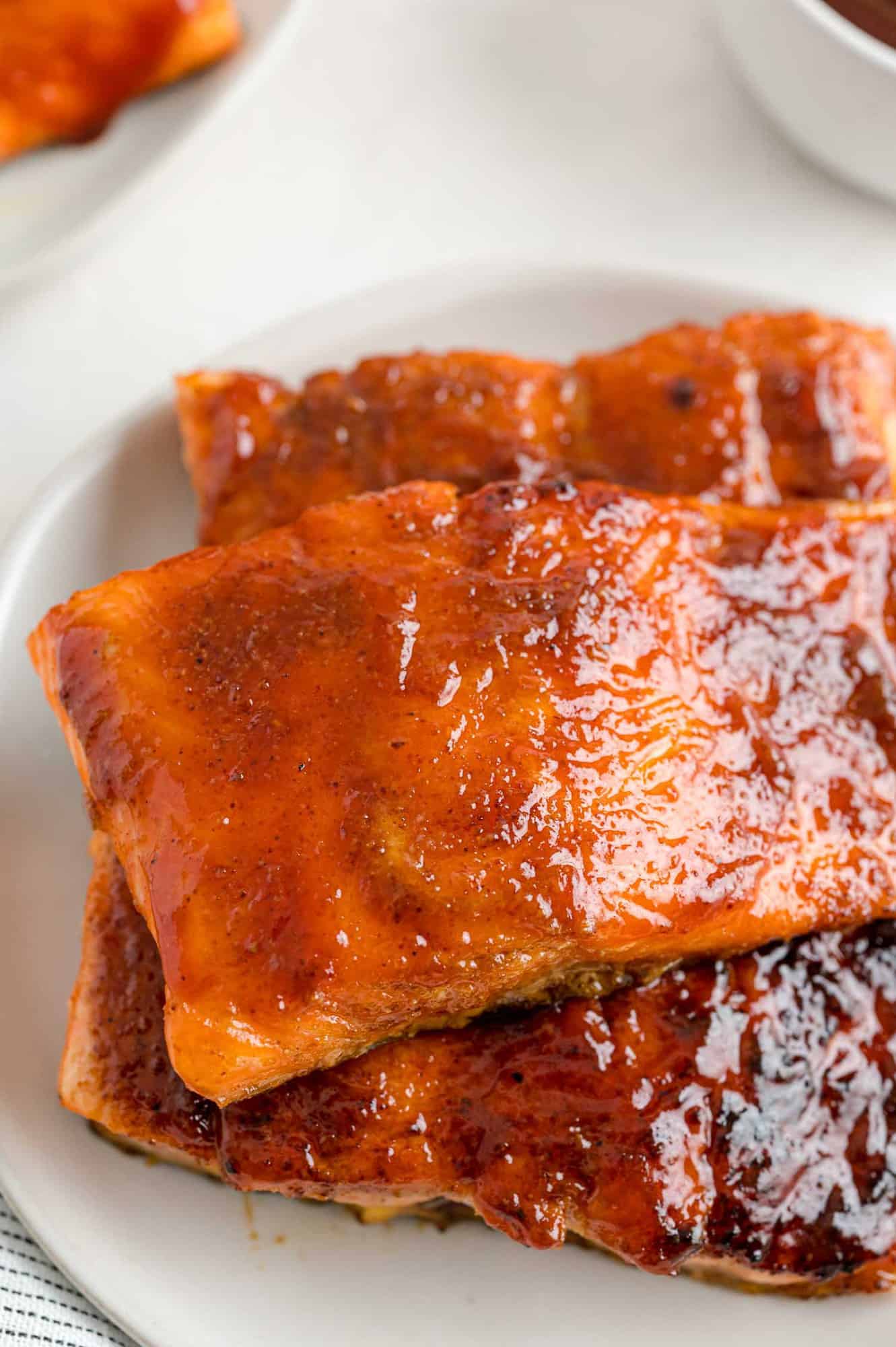 BBQ salmon fillets stacked on a white plate.