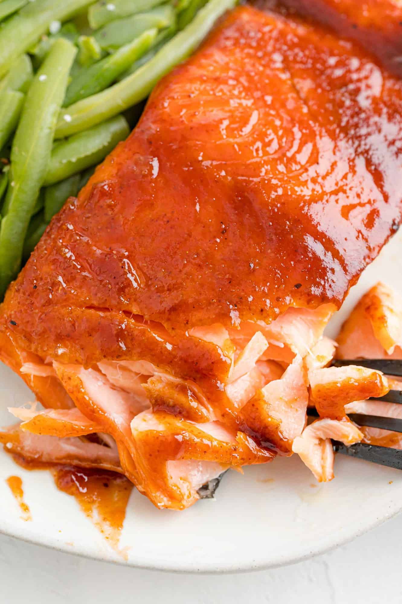 BBQ salmon next to green beans on a plate, flaked with a fork to show the texture.