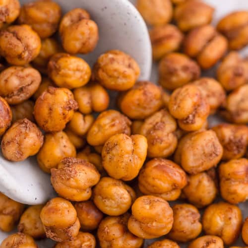 Close up of roasted chickpeas with cinnamon spilling out of a white scoop.