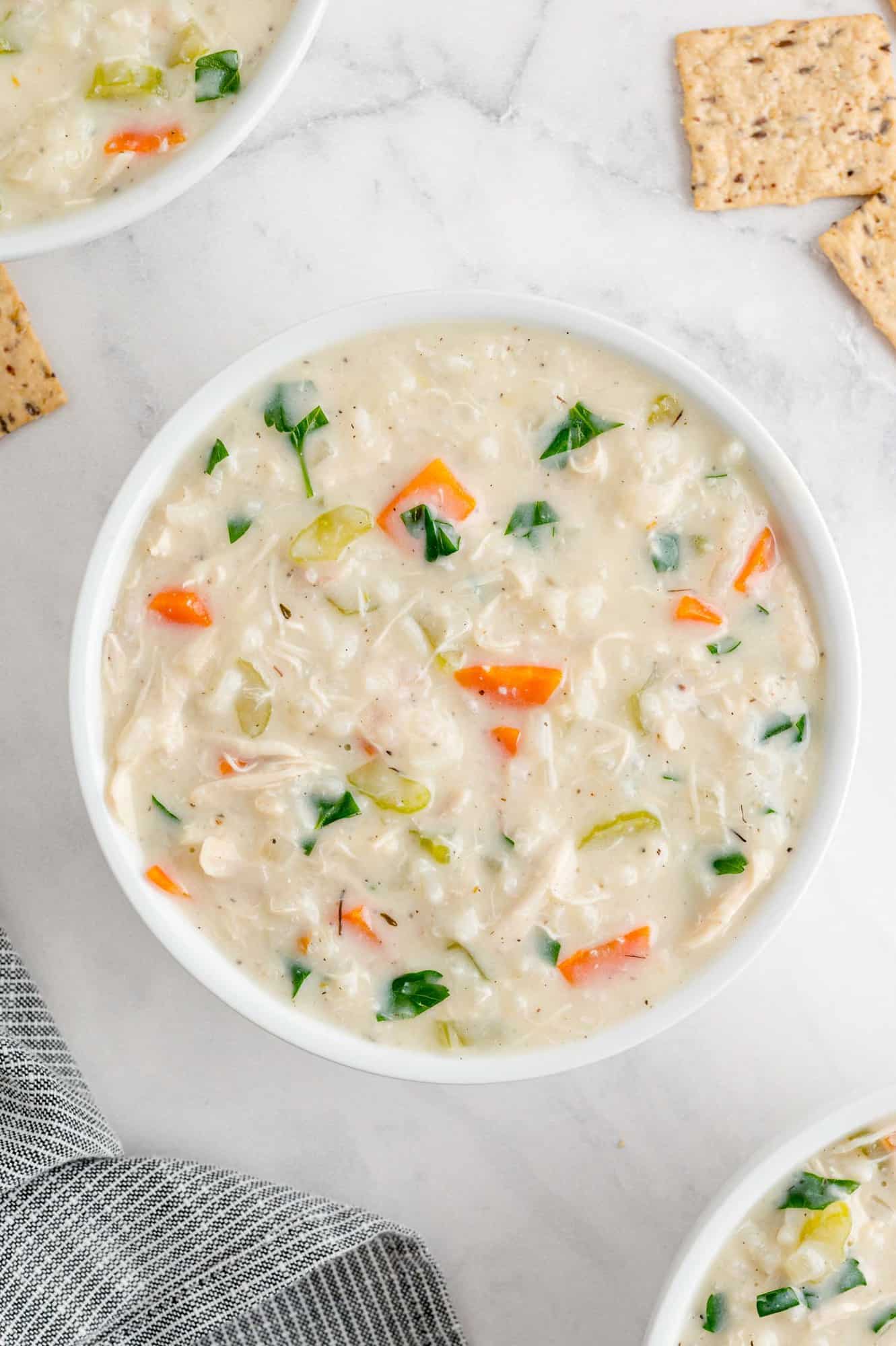 Bowl of creamy chicken rice soup, two other bowls partially visible.