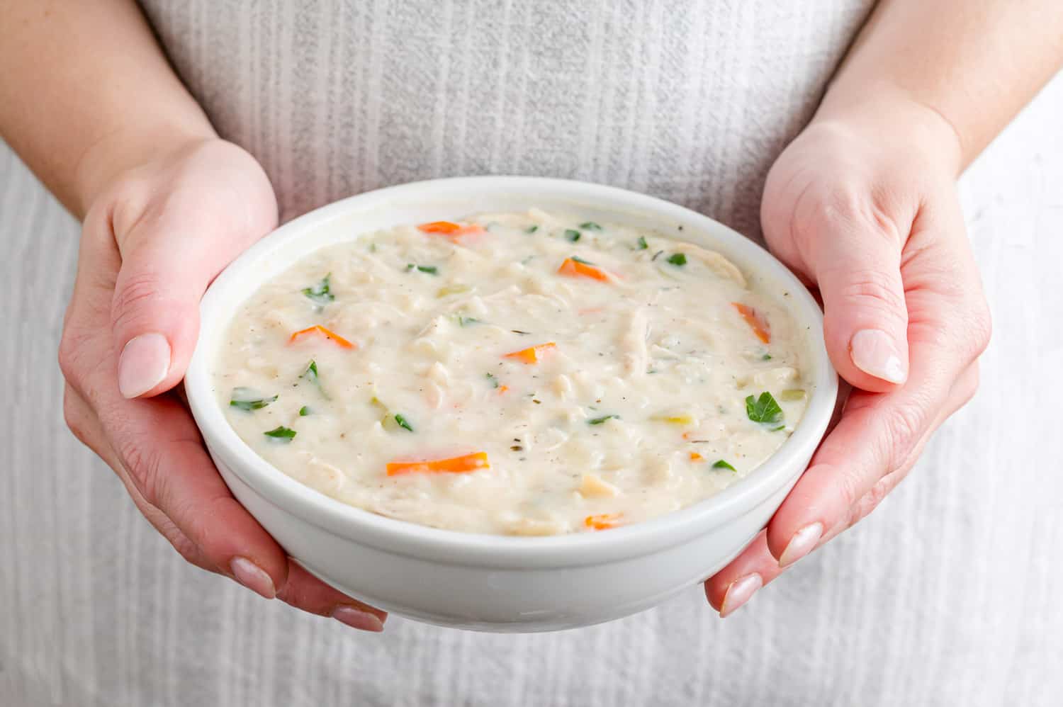 Two hands holding a bowl of soup.