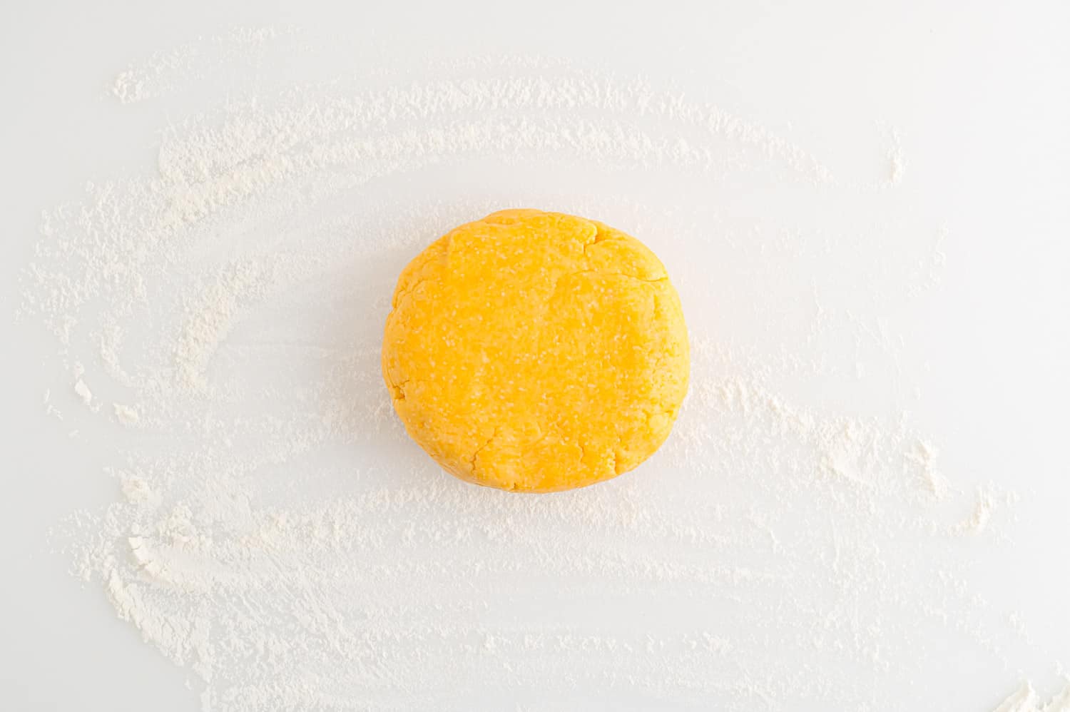 A round ball of yellow dough sits on a lightly floured white surface.