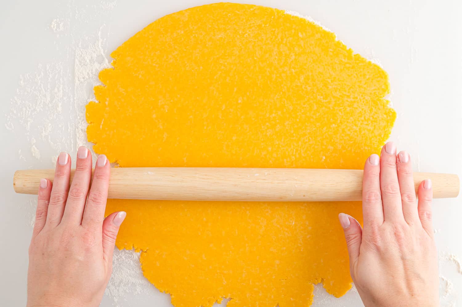 Dough being rolled out with a wooden rolling pin.