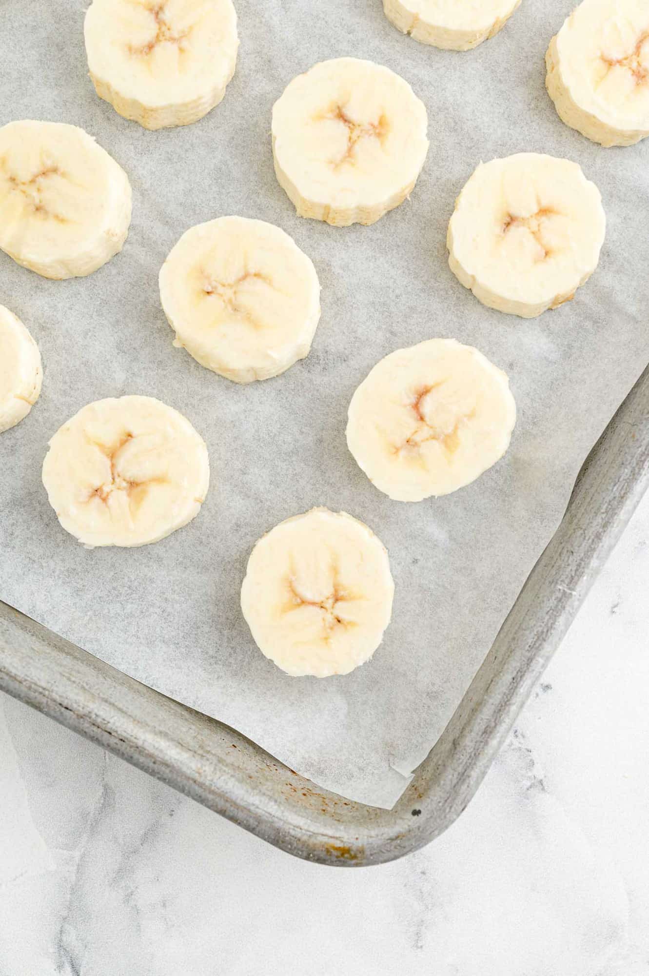 Sliced bananas on a sheet pan lined with parchment.