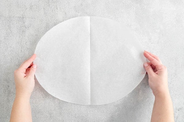 Two hands holding an unfolded parchment paper oval.