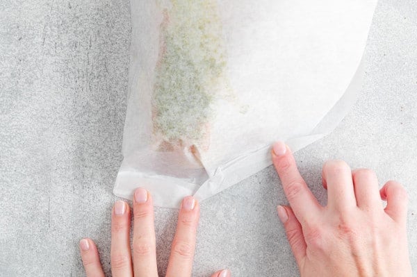 One hand holding the parchment paper packet closed while the other hand folds over the edge to seal.