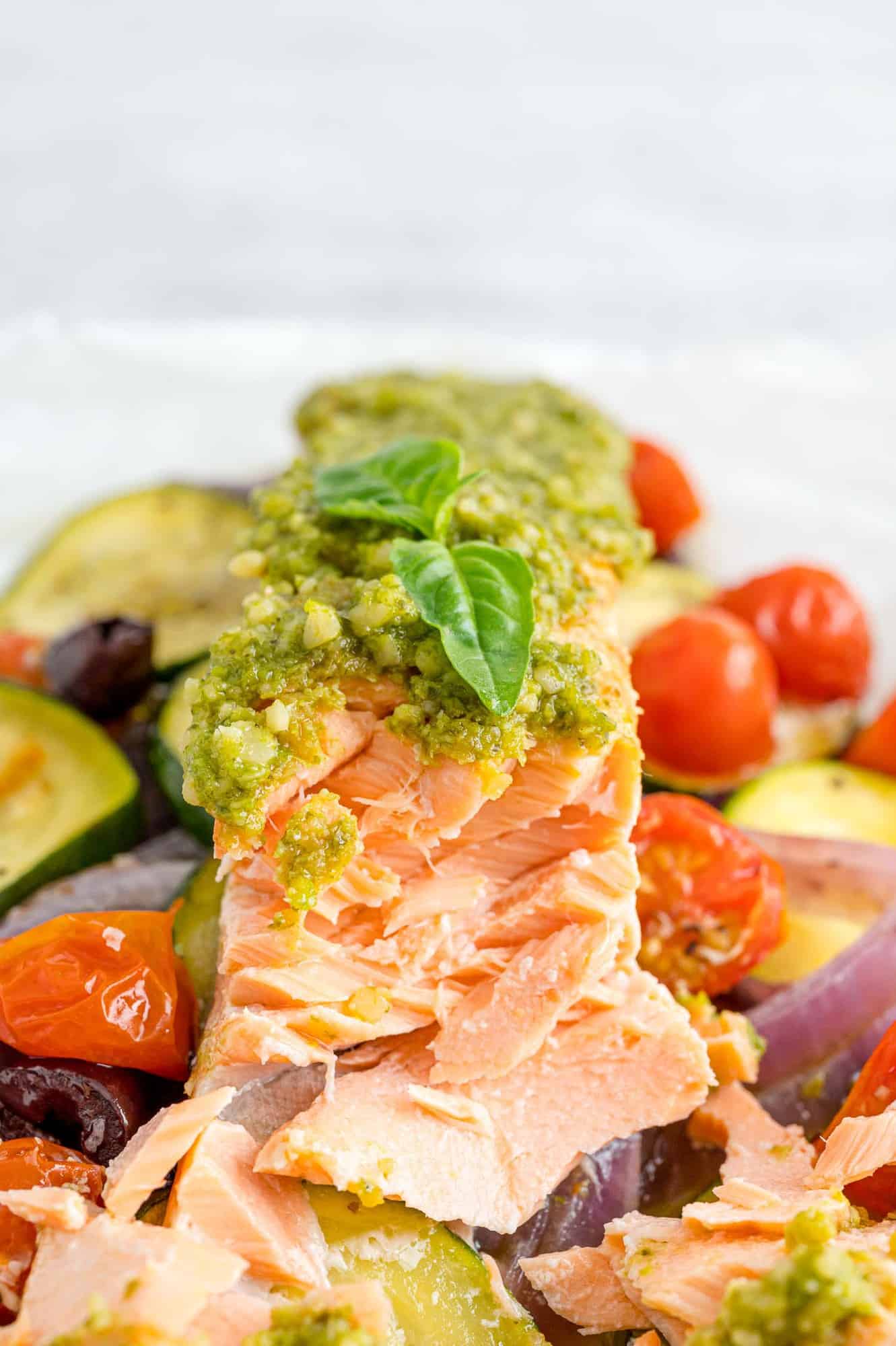 Pesto salmon on a bed of vegetables, flaked to show the texture.