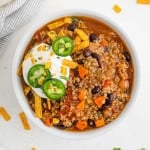 Round bowl of quinoa chili with black beans, garnished with sour cream and jalapeno.
