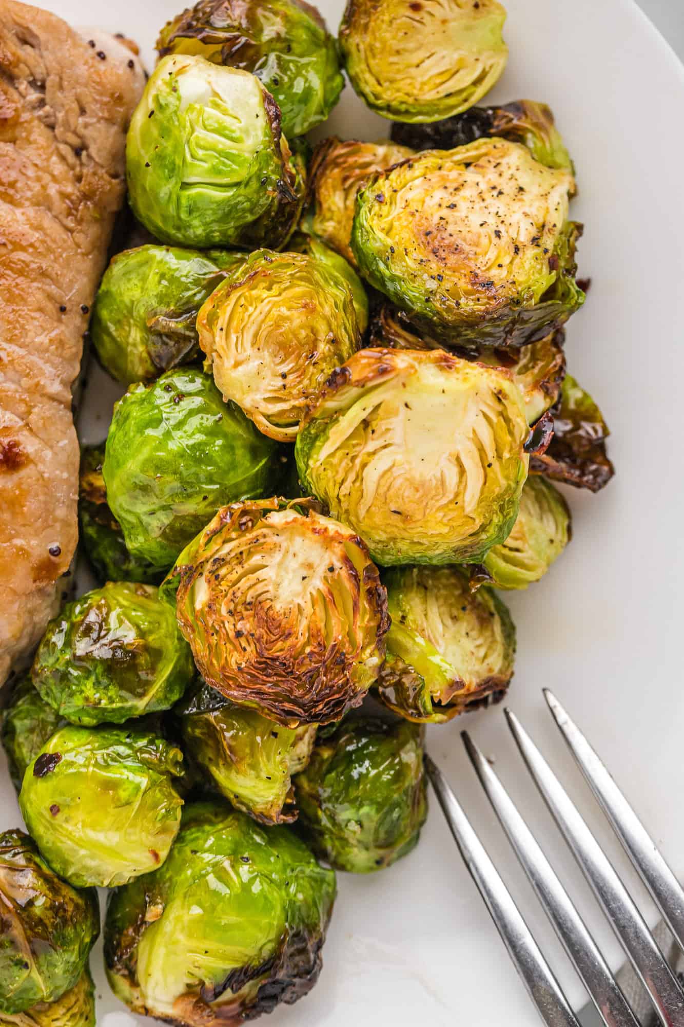 Close up of air fried brussels sprouts on a plate with a pork chop.