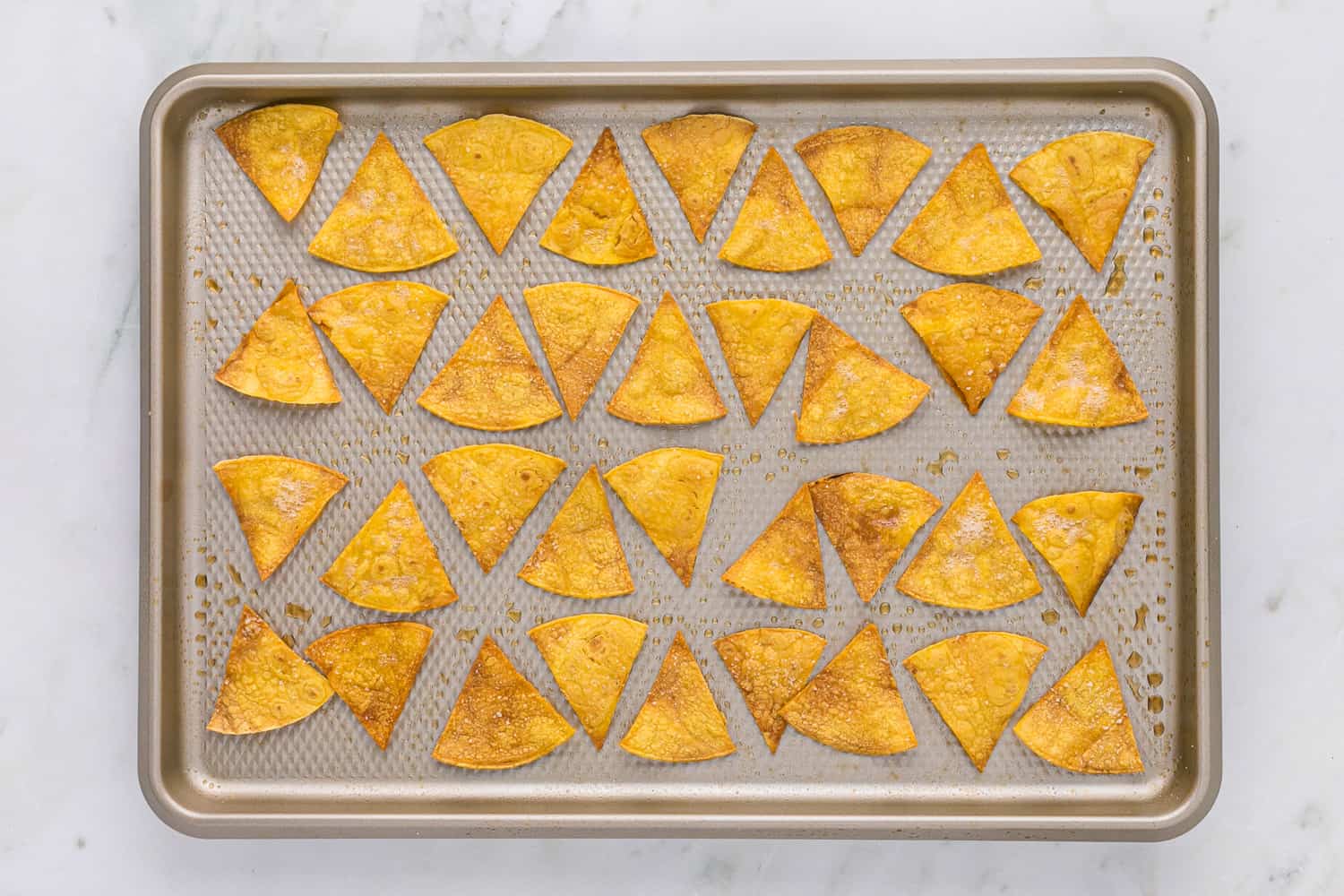 Baked tortilla chips on a baking sheet.