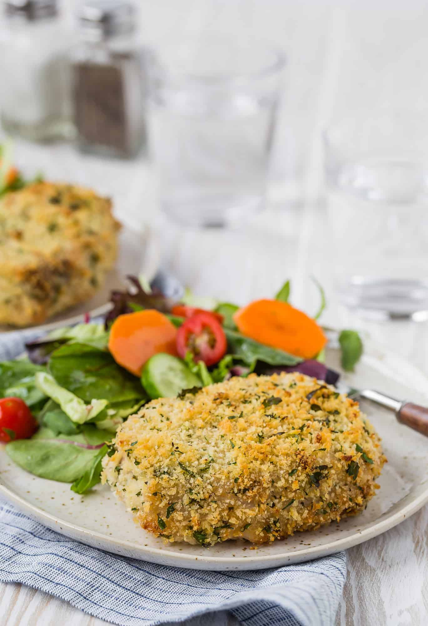 Golden brown baked pork chop on a small plate with green salad.