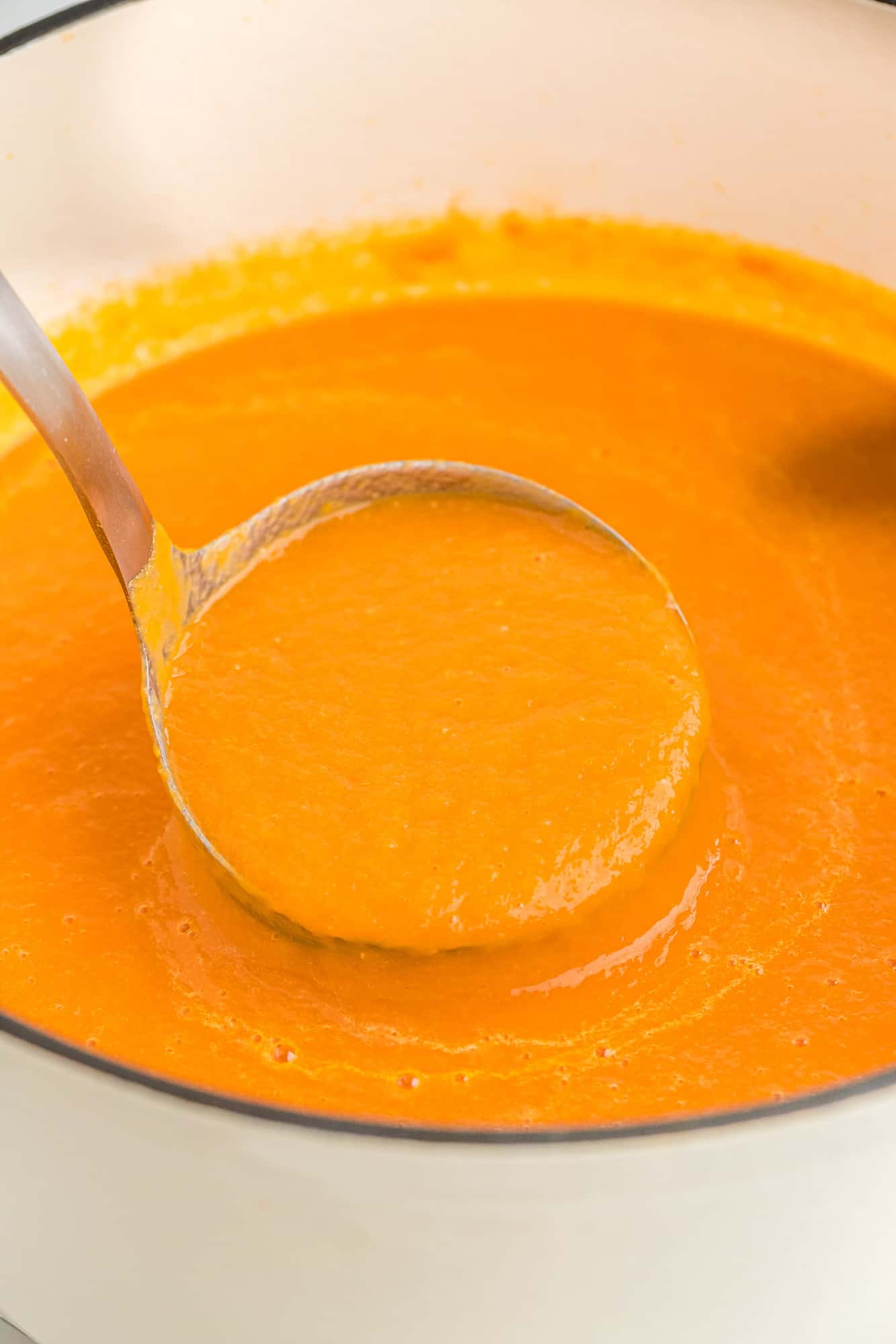 Smooth orange soup in a ladle.