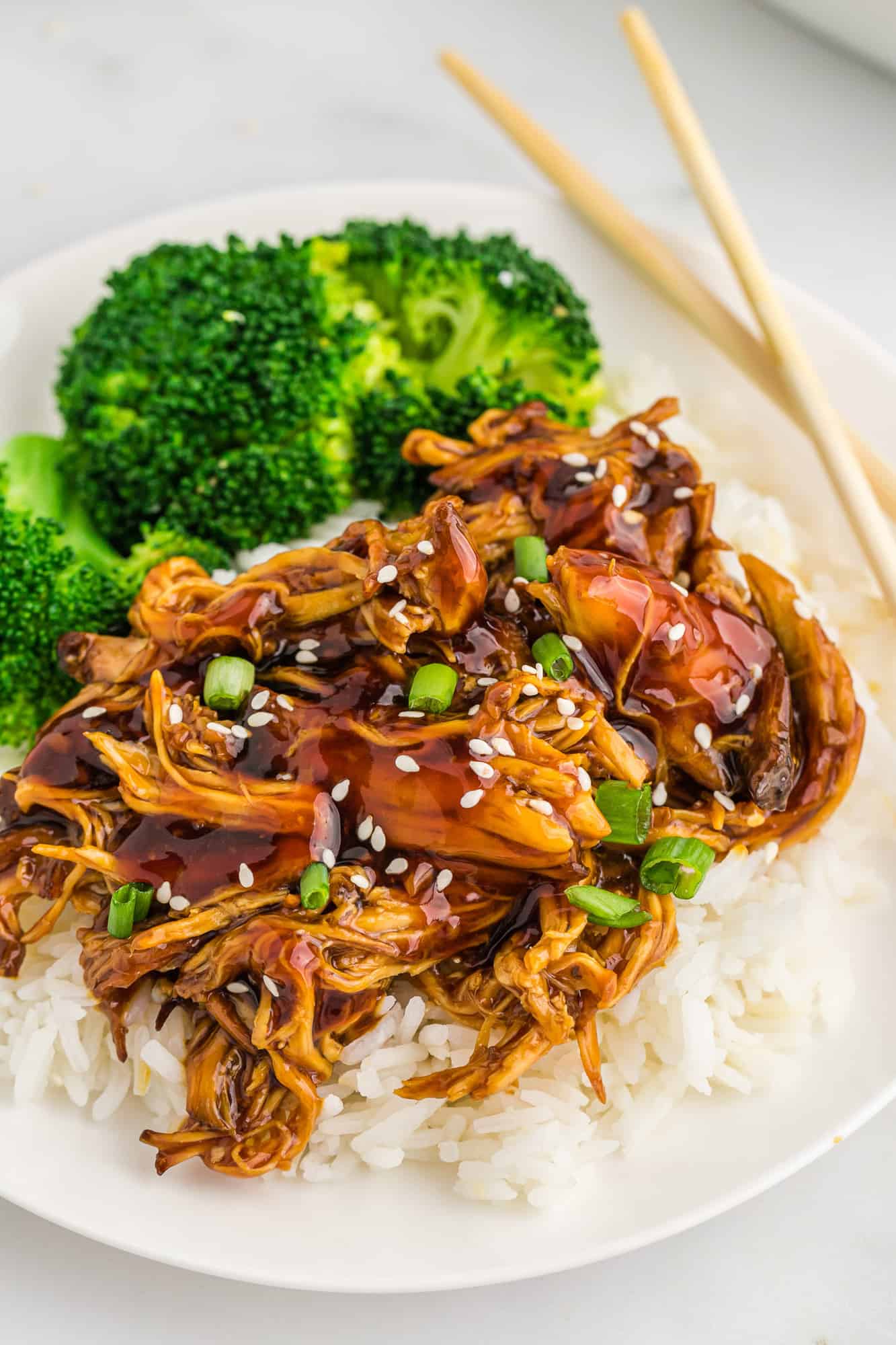 Close up of glazed shredded chicken on a plate with steamed broccoli and rice.