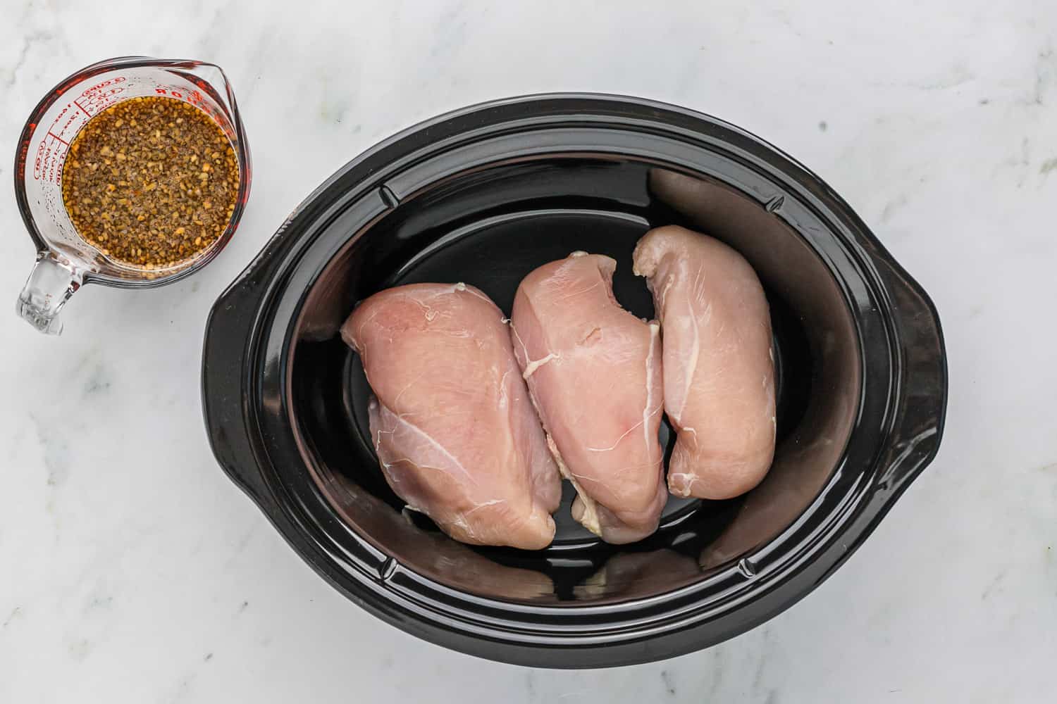 Chicken breasts in a black slow cooker.