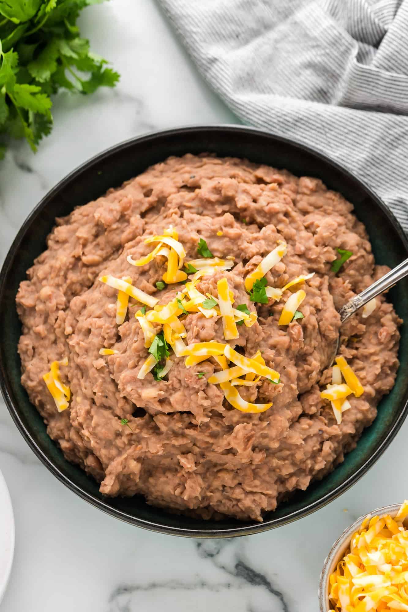 Overhead view of large bowl of crockpot refried beans with cheese and cilantro.