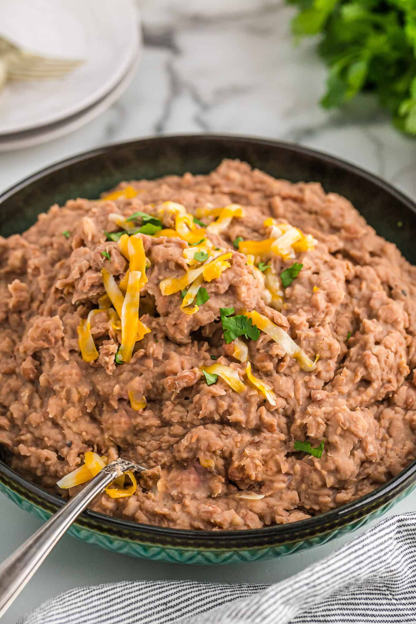 Slow cooker refried beans are fat free "refried" beans made in the slow cooker. Easy and way better tasting than the stuff in a can! Crockpot refried beans topped with cheese and cilantro.