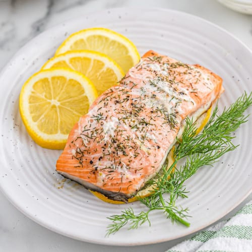 Salmon on a white plate with lemon slices and fresh dill.
