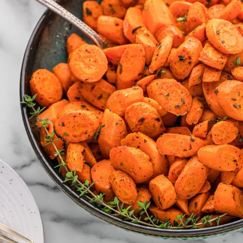 Roasted carrots in a dark colored bowl with a silver spoon.