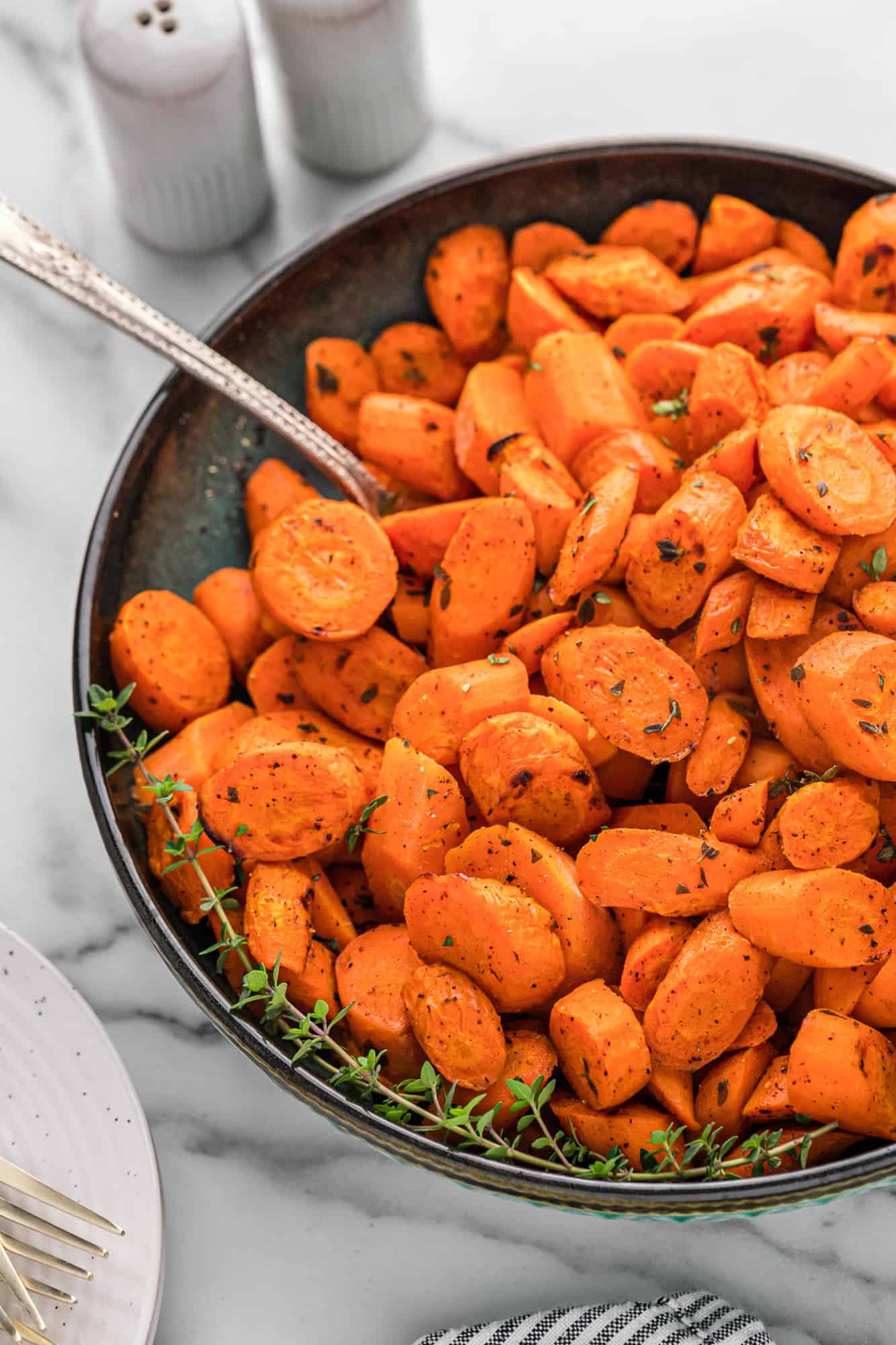 Large bowl of roasted carrots with thyme, and a serving spoon.