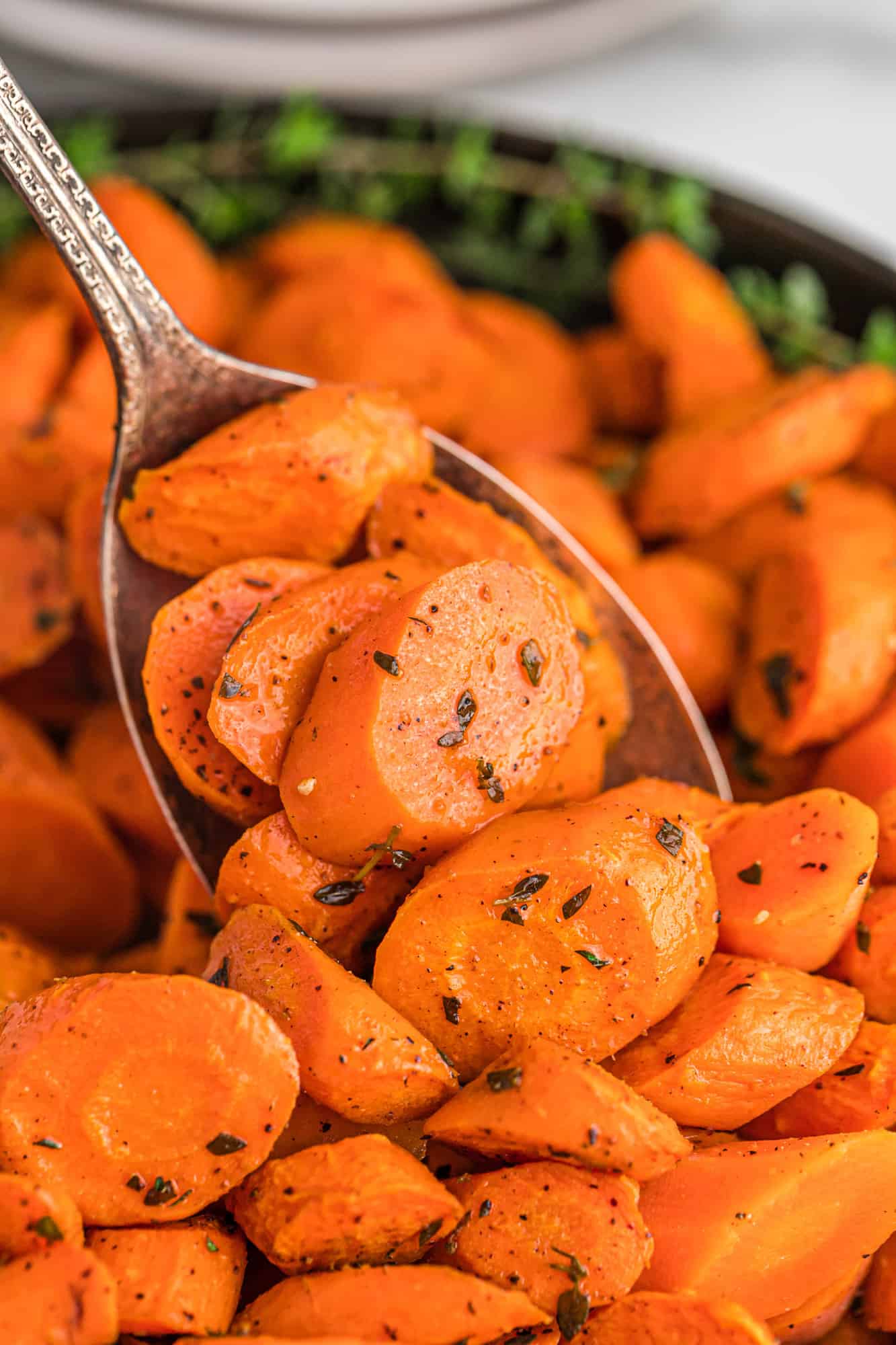 Close up of roasted carrot slices on serving spoon, sprinkled with fresh thyme leaves.