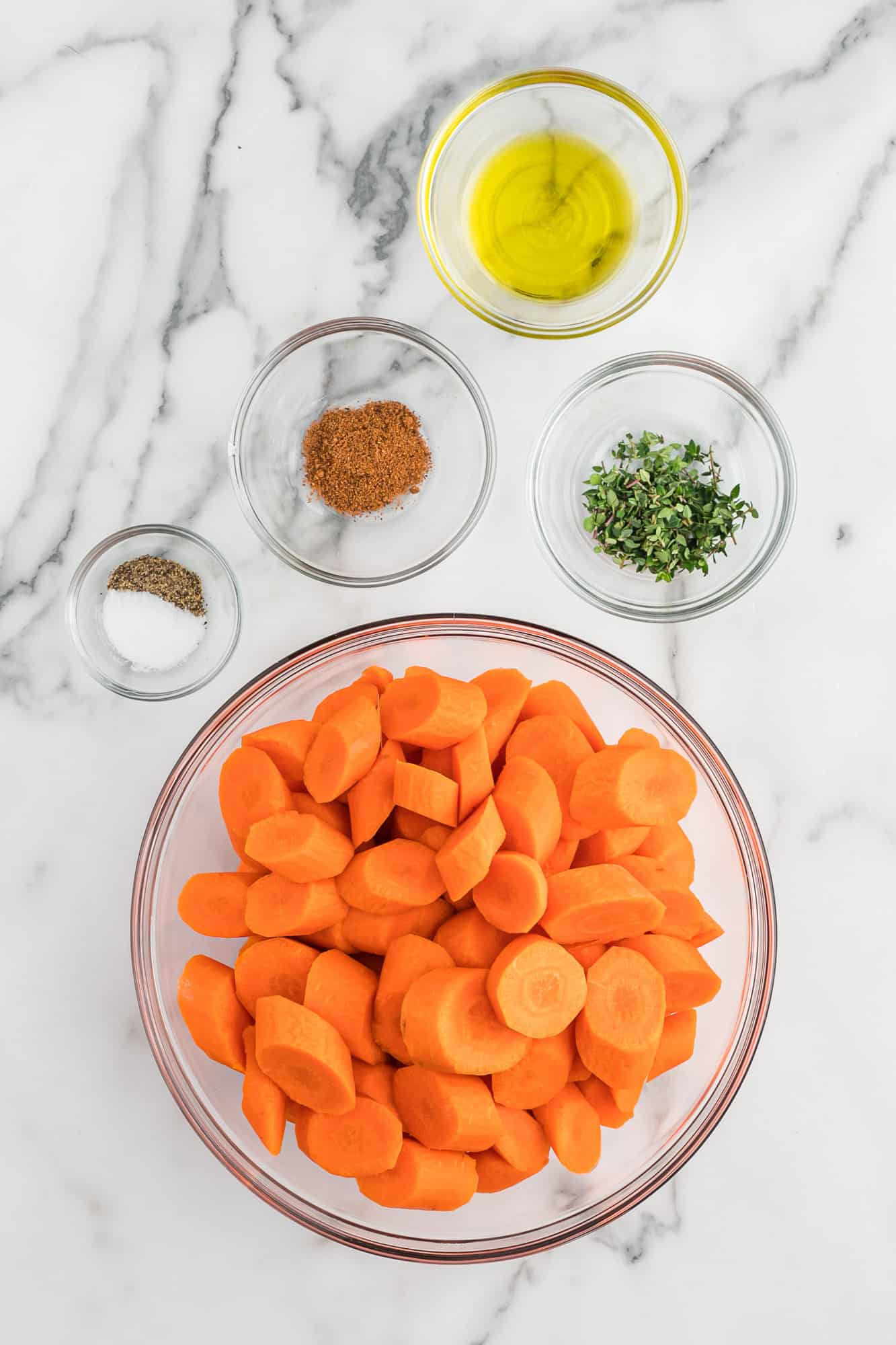 Overhead view of ingredients needed for recipe, sliced carrots, nutmeg, thyme, olive oil, salt & pepper.