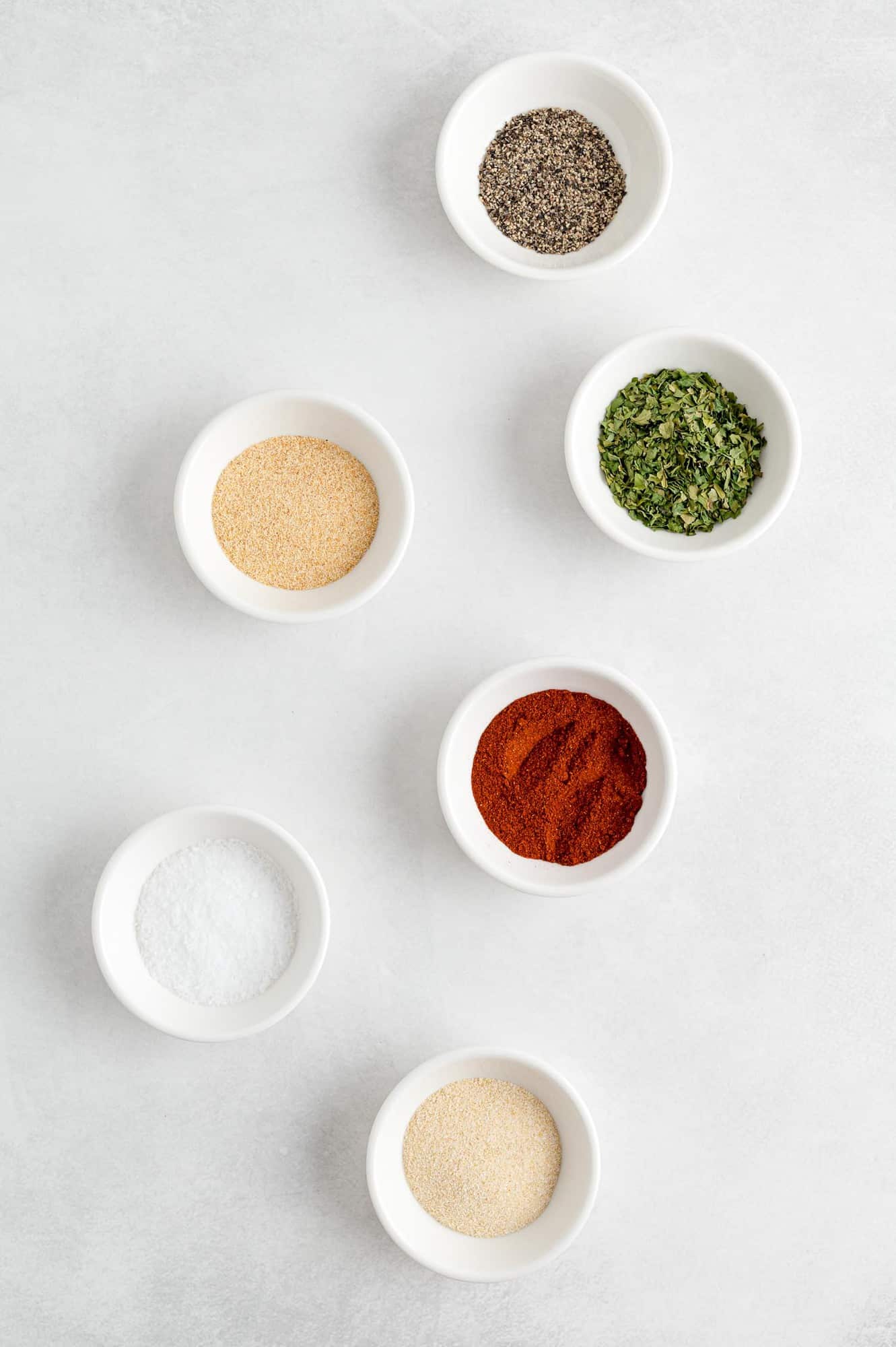 Overhead view of individual spices in small white bowls.