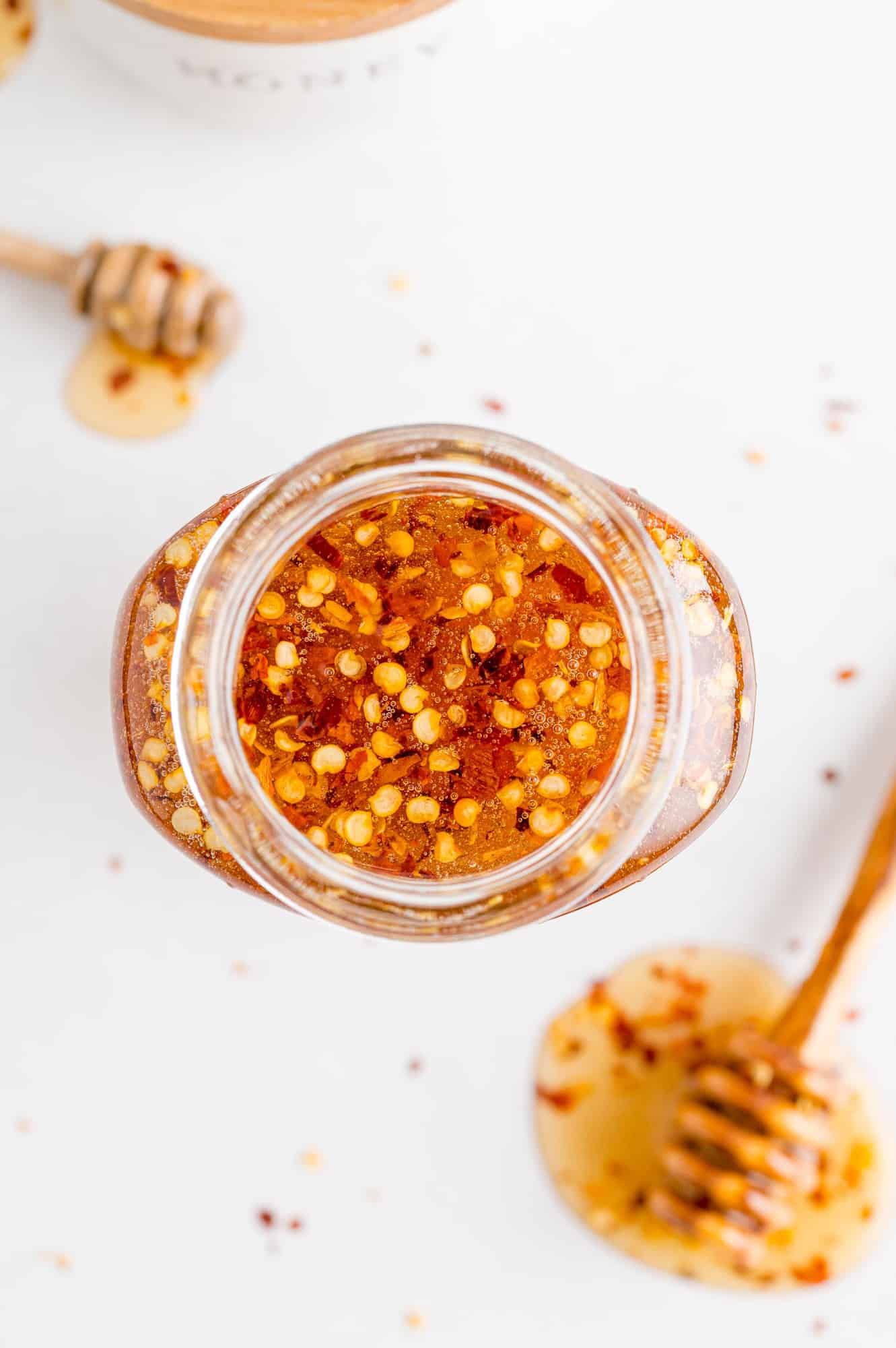 Overhead view of hot honey in a jar and on a dipper on white surface.